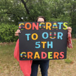Teacher holding up handmade poster with Congrats to our 5th graders"